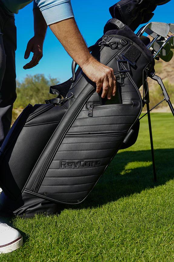 Golfer lifting a RevCore hybrid stand golf bag on a sunny fairway.